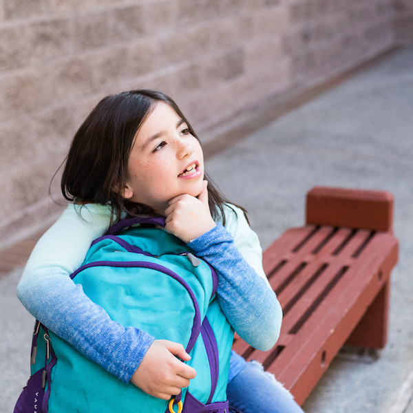 Girl sitting on park bench with backpack thinking deeply