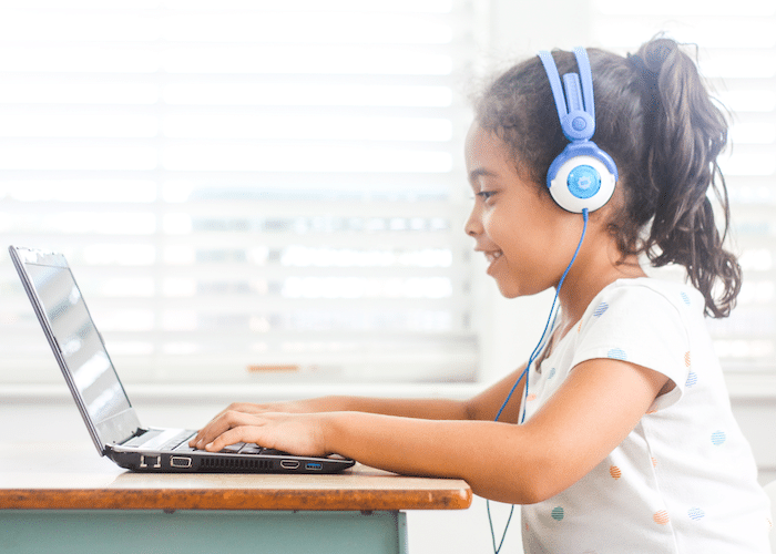 Photo of smiling girl participating in online learning activity at a laptop with headphones on
