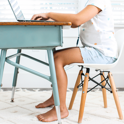 Child sitting at teal desk with bare feet typing on laptop and working toward earning virtual incentives