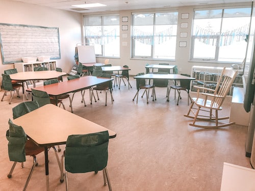 Image showing classroom set up with tables to encourage classroom community building. Classroom with tables, chairs, seat sacks, rocking chair and windows.