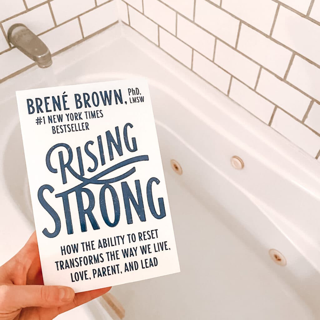 Holding the book "Rising Strong" by Brene Brown and running a bath for my Sunday routine relaxation