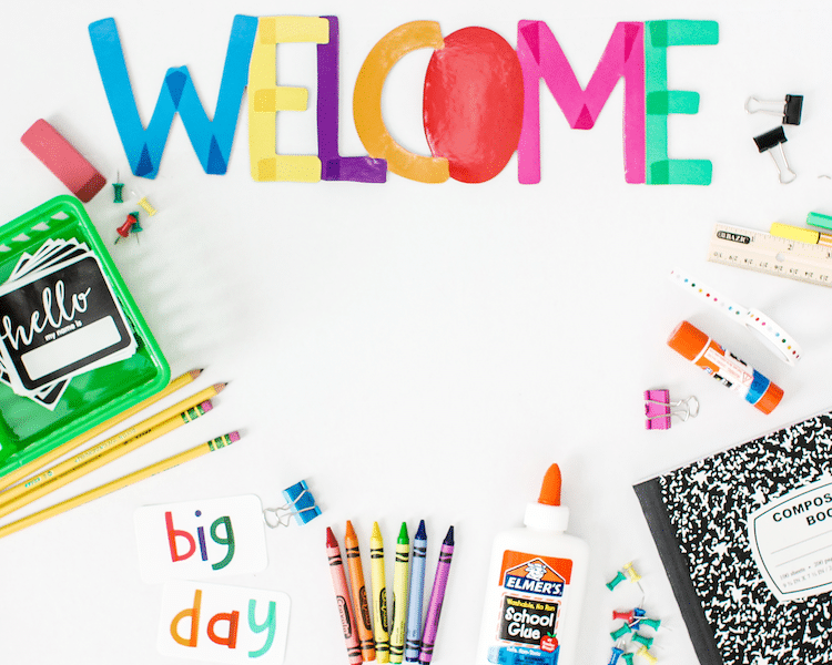 Flat lay back to school photo with welcome sign, glue stickers, composition notebook, crayons, etc.