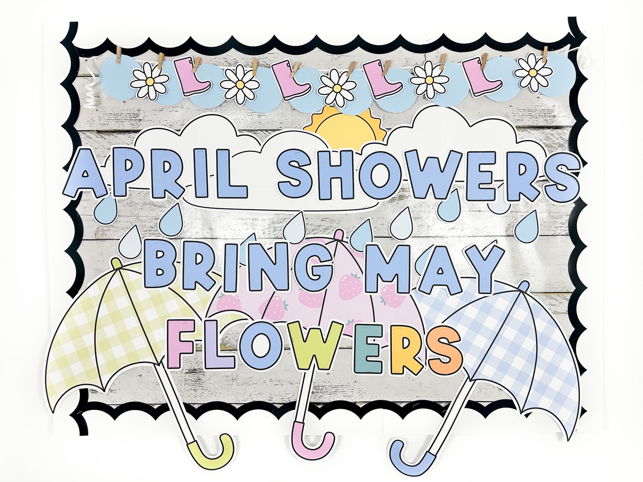 Spring bulletin board with message "April showers bring may flowers" with three large umbrellas, raindrops, clouds and a sunshine