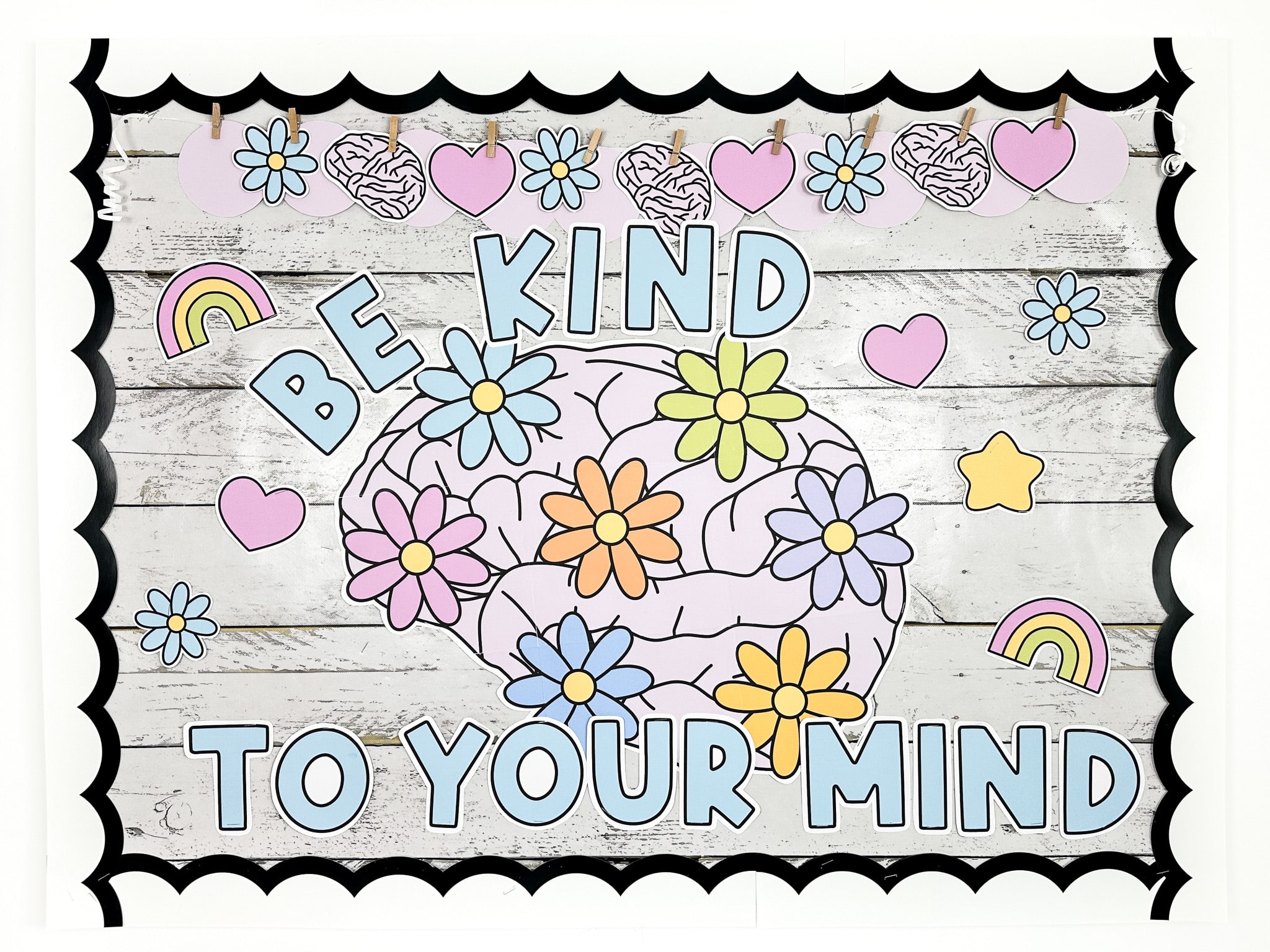 Mental health bulletin board with a large brain with daisies on it with small stars, hearts, and rainbows around the message "Be Kind to your Mind"